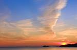 Stock photo of a sunset over Agawa Bay on Lake Superior in Lake Superior Provincial Park, Ontario, Canada. The sun is a small yellow ball just at horizon level, surrounded by bright red that fades to hues of orange and yellow. There is blue sky streaked w
