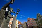 Stock photo of Bronze statue of a jester atop a fountain back dropped by the colorful facades of buildings in the Old Town district in the City of Landshut, Bavaria, Germany, Europe.