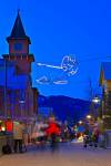 Stock photo of decorative lighting and pedestrian activity along the Village Stroll at dusk, Whistler Village, British Columbia, Canada. The sky above is a gorgeous deep blue over this active Winter scene showing people moving about and a skier made of li