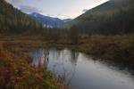 Stock photo of snow capped peaks of the Selkirk Mountains and fall forest colors viewed from beside a natural pond in the Slocan Valley, Central Kootenay, British Columbia, Canada.