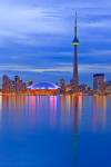 Stock photo of the Toronto city skyline illuminated at dusk, highlighting the CN Tower and Rogers Centre on the waterfront shore of Lake Ontario, Ontario, Canada.