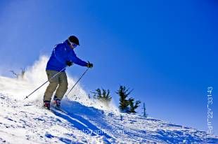 Stock photo of a skier on the upper slopes of Whistler Mountain against a clear blue sky at the Whistler Blackcomb ski resort in Whistler, British Columbia, Canada. 