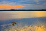 Stock photo of a person riding in a canoe enjoying a lovely yellow-gold sunset on the beautiful Lake Audy in Riding Mountain National Park, Manitoba, Canada.