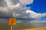 Stock photo of a yellow caution sign on the sandy shores of Lake Winnipeg with threatening clouds above in the town of Winnipeg Beach, Manitoba, Canada.