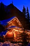 Stock photo of a snow covered log cabin lit up in this winter night scene on the shores of Lake Louise in Banff National Park in the Canadian Rocky Mountains, Alberta, Canada. A beautiful blue night sky silhouettes the mountains behind this cabin.