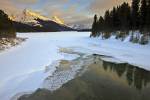 Stock photo of the partially frozen Maligne River as it drains from Maligne Lake during winter with a view towards the snow capped mountains of Leah Peak (2810 metres/9220 feet) and Samson Peak (3077 metres/10095 feet) during sunset, Maligne Lake Road, Ja