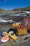 Stock photo of a wicker picnic hamper beside a waterfall with a helicopter in the background in the Mealy Mountains, Southern Labrador, Labrador, Newfoundland Labrador, Canada.