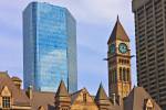 Stock photo of the clock tower at the Old City Hall Building with modern buildings and blue sky in the background.