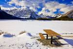 Stock photo of a picnic table on the shore of the frozen, snow covered Upper Kananaskis Lake during winter, backdropped by the Kananaskis Range in Peter Lougheed Provincial Park in Kananaskis Country, Canadian Rocky Mountains, Alberta, Canada. 