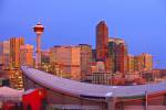 Stock photo of the Saddledome with high-rise buildings and the Calgary Tower in the background at sunrise, City of Calgary, Alberta, Canada. This attractive skyline is backdropped by a clear blue sky and many of the buildings still have their nighttime li