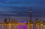 Stock photo of the City of Toronto's skyline with the CN Tower and Rogers Centre all lit up and reflecting onto Lake Ontario taken near nightfall.