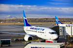 Stock photo of a WestJet Boeing 737-600 aircraft on the apron at the Calgary Airport with the buildings of downtown Calgary in the background, City of Calgary, Alberta, Canada. The sky is striped with bands of thick white clouds and clear blue sections. 