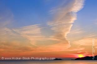Stock photo of a sunset over Agawa Bay on Lake Superior in Lake Superior Provincial Park, Ontario, Canada. The sun is a small yellow ball just at horizon level, surrounded by bright red that fades to hues of orange and yellow. There is blue sky streaked w