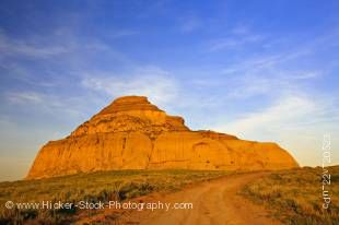 Stock photo of a dirt road leading to magnificent Castle Butte during sunset in the Big Muddy Badlands, Southern Saskatchewan, Canada.