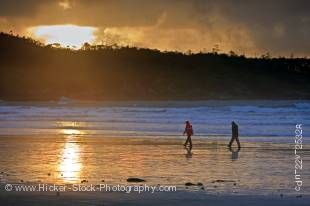 Stock photo of a couple walking along the beach at Cox Bay near Tofino during sunset on the west coast of Vancouver Island in British Columbia, Canada.