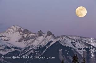 Stock photo of a full moon at dusk shining over the snowcapped Fairholme Range during winter, as seen from 2nd Vermilion Lake near the town of Banff in Banff National Park, Canadian Rocky Mountains, Alberta, Canada.