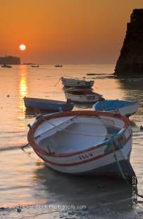 Stock photo of a small fishing boat at a golden sunset on the Playa de la Caleta in Cadiz, Spain.