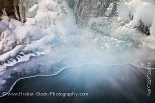 Stock photo of a partially frozen Lower Falls of the Johnston Creek during winter with water flowing into a pool at the base, surrounded by ice formations, Johnston Canyon, Banff National Park, Canadian Rocky Mountains, Alberta, Canada. 
