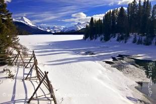 Stock photo of a partially frozen Maligne River and a wooden fence under a blue sky during winter as the river drains from Maligne Lake, with a view towards Samson Peak from along Maligne Lake Road, Jasper National Park, Canadian Rocky Mountains, Alberta,
