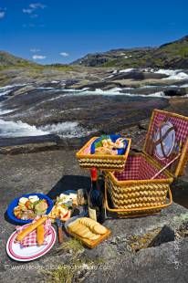 Stock photo of a wicker picnic hamper beside a waterfall with a helicopter in the background in the Mealy Mountains, Southern Labrador, Labrador, Newfoundland Labrador, Canada.