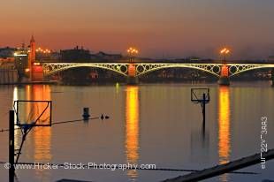 Stock photo of the lighted Puente de Isabel II Bridge across the Rio Guadalquivir River at dusk, City of Sevilla, Province of Sevilla, Andalusia, Spain, Europe.