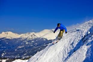 Stock photo of a skier on the upper slopes of Whistler Mountain, Whistler Blackcomb, Whistler, British Columbia, Canada. Numerous mountain slopes can be seen in the background of bright blue sky.