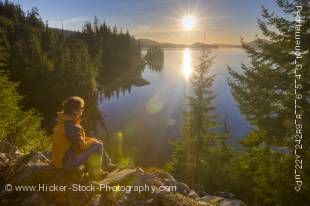 Stock photo of a woman tourist sitting on a rocky ledge overlooking the nature of Tofino Inlet, Vancouver Island, British Columbia, Canada.